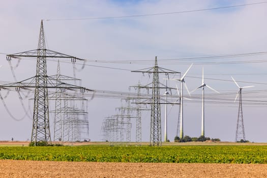 Panorama with countless power poles and power lines next to a solar farm with wind turbines in the countryside