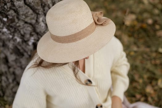 A young beautiful woman in a dress and a round hat reads a book outdoors in the forest and drinks tea. Romantic and vintage photo of a beautiful girl. Reading and relaxation