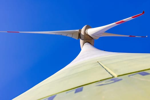 Rotor with nacelle and blades of a wind turbine with tower and shaft seen from below against blue sky