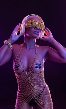 Hipster fashion girl, african american model wear headphones enjoy listen new cool music mix. Woman stand at purple studio background in trendy club purple party light with fog
