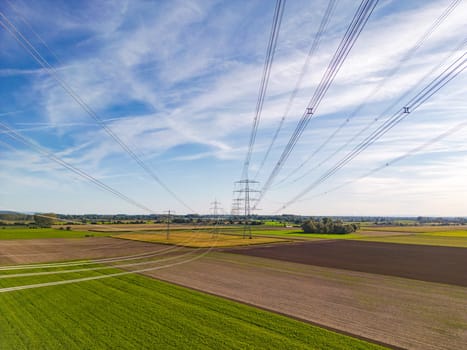 Rural nature landscape in conflict with artificial structures of power poles and power lines for energy for the consumer society as aerial shot