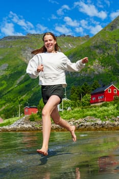 Young girl teenager running on beach in Norway Fjord. Vacation in Nordland in summer.