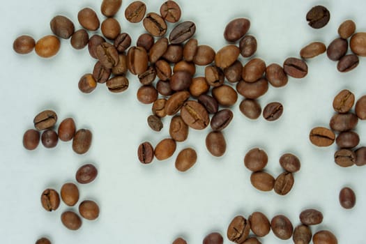 Roasted coffee beans randomly scattered across a light background, creating a simple and natural composition emphasizing texture and organic qualities.