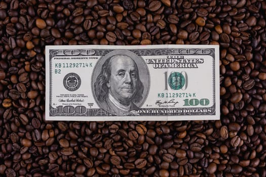 A one hundred dollar bill placed on a surface of roasted coffee beans, representing the cost of coffee, trade, or financial concepts.