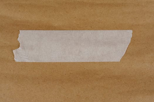 Torn white adhesive tape placed on a textured brown kraft paper surface, offering a creative design element for crafting, scrapbooking, or branding projects.