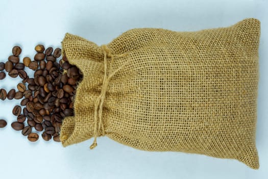 Top view of a burlap sack spilling roasted coffee beans onto a white background, highlighting natural packaging and rich texture.
