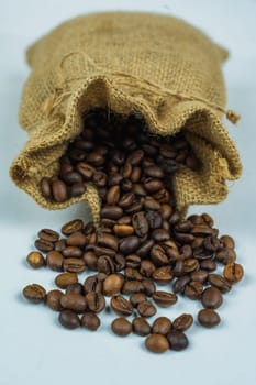 Close-up view of roasted coffee beans spilling out of a burlap sack onto a white background, showcasing texture and natural packaging.