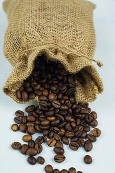 Burlap sack filled with roasted coffee beans spilling onto a white background, highlighting the rustic texture and natural packaging.