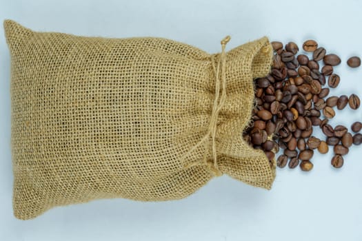 Overhead view of a burlap sack with roasted coffee beans spilling onto a white surface, highlighting natural material and coffee texture.