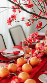 A sophisticated lunar new year table features elegant red and gold tableware, mandarin oranges, and blooming branches as a centerpiece in a stylish modern interior. the minimalist setup reflects tradition and contemporary design.