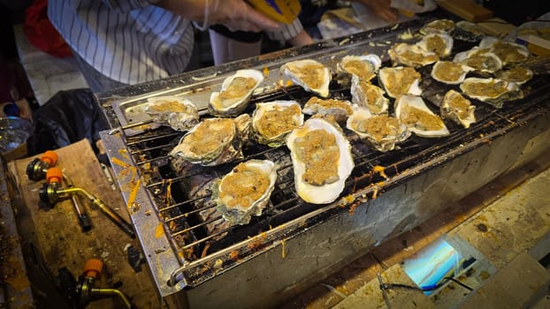 street vendor uses a torch flame to prepare delicious grilled oyster with flair and skill, showcasing the vibrant atmosphere of bustling night Thai markets. Good for recipe book