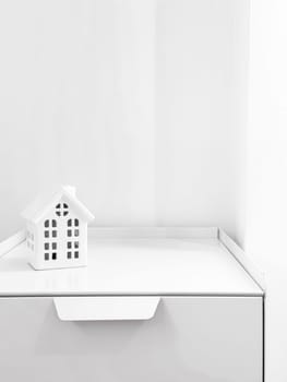 Minimalist white house model on a white shelf with bright lighting.