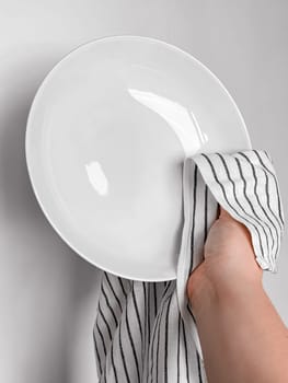 Hand drying white ceramic plate with striped cloth in kitchen setting.
