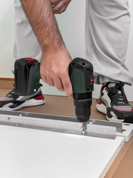 Young caucasian male assembling furniture using power drill.