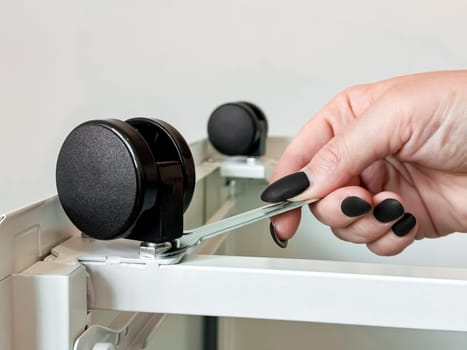 Female hand adjusting caster wheel on office furniture with wrench.