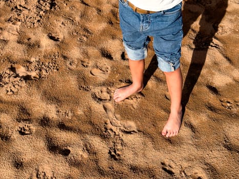 Childs barefoot adventure on sandy beach with rolled up jeans.