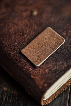 Close-up view of a glossy rectangular sticker on a textured leather journal, the contrast between the shiny sticker surface and the matte leather texture. ideal for branding, stationery design, and product presentation themes.