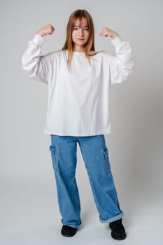 A joyful young girl with long hair wearing a white sweater stands against a plain background close up