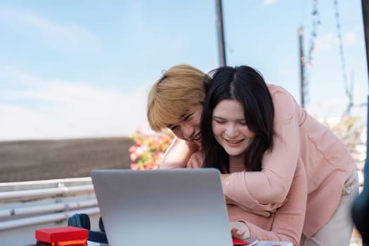 A loving couple shares a joyful moment while engaging with a laptop celebrating their bond in a bright rooftop setting.