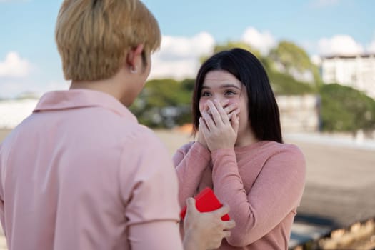 A couple shares a heartfelt moment as one surprises the other with a Valentine proposal outdoors.