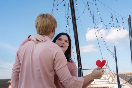 A couple joyfully celebrates Valentine Day outdoors holding a heart surrounded by twinkling lights.