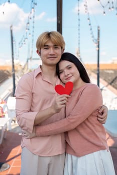 A couple joyfully celebrates Valentine Day on a rooftop capturing a heartfelt moment with a red heart symbol.