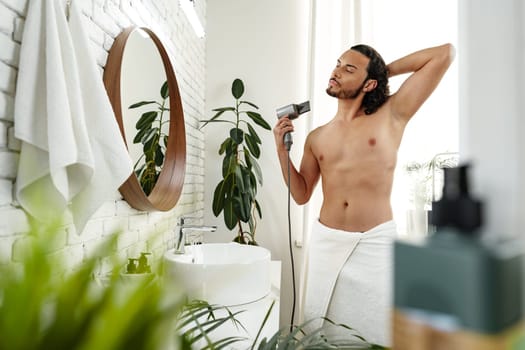 A man with curly hair styles himself in a bright room while using a hairdryer to enhance his look close up