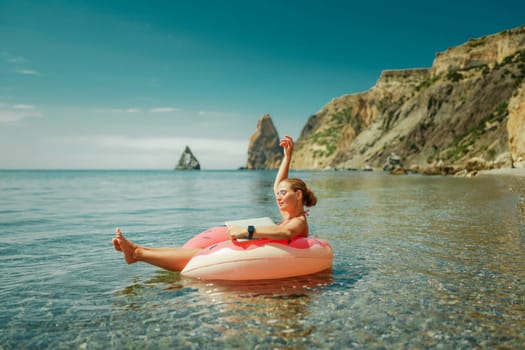 Woman laptop sea. Freelancer woman in sunglases floating on an inflatable big pink donut with a laptop in the sea. People summer vacation rest lifestyle concept
