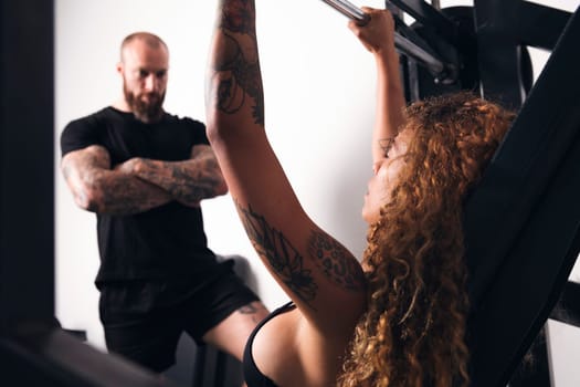 unrecognizable strong sportswoman lifting heavy barbell with weights during functional workout with instructor in gym, concept of fitness and active lifestyle