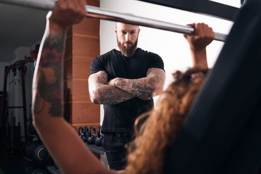 unrecognizable strong sportswoman lifting heavy barbell with weights during functional workout with instructor in gym, concept of fitness and active lifestyle