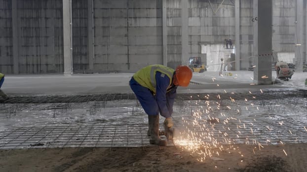 A worker diligently cutting metal in an industrial setting, creating bright sparks, showcasing active construction. Clip