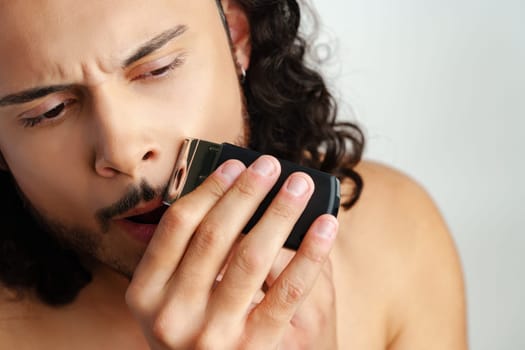 Man trimming his beard indoors using an electric trimmer while showcasing his personal grooming routine close up