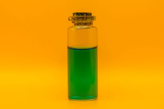Close-up of a small corked glass bottle containing vibrant green liquid, isolated against a bright yellow background.