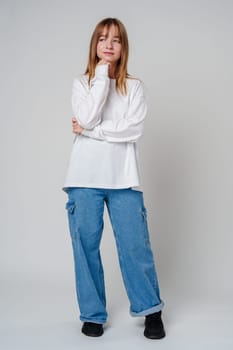 Young woman in a white long-sleeve shirt thoughtfully poses with a hand on her chin in a minimalistic indoor setting