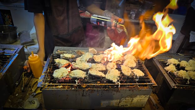 street vendor uses a torch flame to prepare delicious grilled oyster with flair and skill, showcasing the vibrant atmosphere of bustling night Thai markets. Good for recipe book