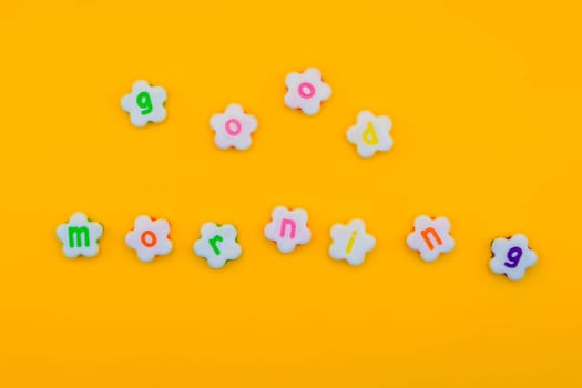 Cheerful "Good morning" spelled out using colorful flower-shaped letters on a bright yellow background, conveying positivity and a fresh start.