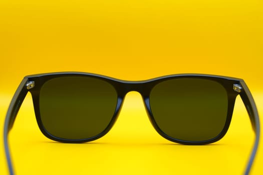 A close-up back view of black sunglasses with dark lenses, displayed against a vibrant yellow background, emphasizing minimalist design and summer style.
