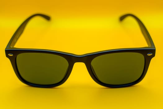 A minimalist display of black sunglasses with dark lenses, set against a bright yellow background, symbolizing summer fashion and modern style.