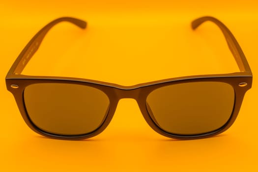 A pair of stylish black sunglasses with dark lenses showcased on a vivid yellow background, highlighting modern fashion and summer vibes.