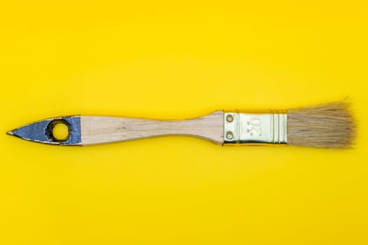 Flat lay of a wooden paintbrush with natural bristles and a metallic ferrule, isolated against a bright yellow background.