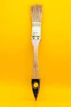 Close-up of a wooden paintbrush with natural bristles and a metallic ferrule, isolated against a bright yellow background.