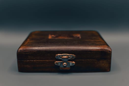 A close-up of an antique wooden box featuring a metal latch and rustic texture, captured against a neutral gradient background.