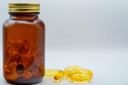 Amber glass bottle filled with Omega-3 capsules, surrounded by scattered yellow capsules on a clean white background, emphasizing health and wellness.