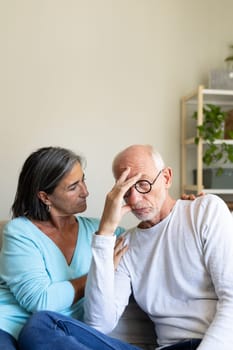 Vertical portrait of mature woman comforting sad man sitting on the couch at home living room. Copy space. Mental health concept.