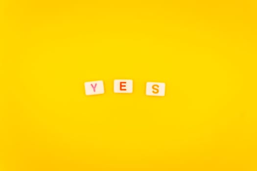Minimalist arrangement of alphabet tiles spelling "Yes" with colorful letters on a bright yellow background, symbolizing affirmation and positivity.