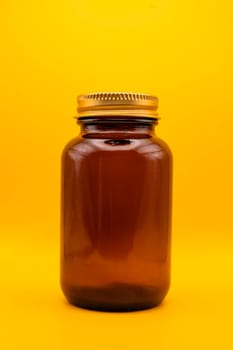 A minimalistic close-up of an amber glass jar with a golden lid, isolated against a bright yellow background, ideal for packaging or branding projects.