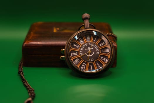 Vintage pocket watch marked "Marine Anchor 1912" with chain displayed on a wooden box, photographed against a green background.