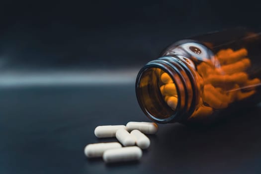 Close-up of a tipped brown glass bottle with white capsules scattered on a dark background, symbolizing healthcare and medication.
