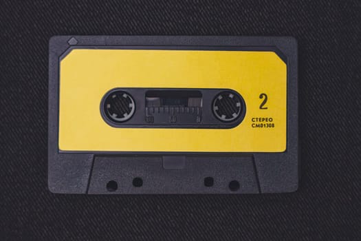 A vintage audio cassette tape in black with a yellow label, featuring stereo marking, captured on a textured dark background for a nostalgic aesthetic.