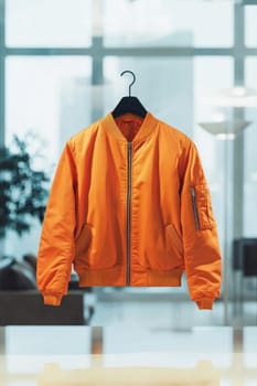 Stylish orange bomber jacket hanging on a black hanger in a modern office, ready for a day at work